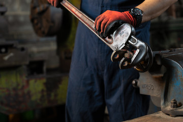 Body shot of maintenance engineer operating an industrial giant pipe wrench on metal that is...