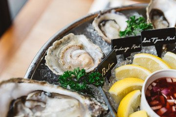 Close up Belon Oyster and many kinds of fresh oysters served in round tray with slice lemon and spicy sauce.