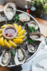 Many kinds of Fresh Oysters served in round tray with slice lemon and spicy sauce.