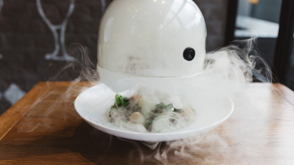 Male hand lifts to up glass cloche from a plate with hot food and moving smoke at the restaurant - Smoked food time! Close Up.