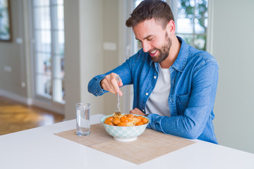 Handsome man eating pasta with meatballs and tomato sauce at home while smiling at the camera