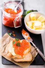 Salmon red caviar in a glass jar and Sandwiches with butter and parsley on slate cutting board on a light marble background. Seafood. Healthy Food Concept. Snack.