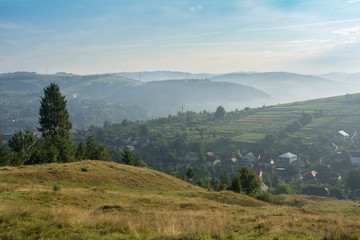 Morning misty landscape: mountain village, mountain slopes, forest.