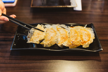 Hand pinching Yaki-Gyoza (Japanese Pan-Fried Dumplings) served on black plate.