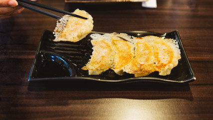 Hand pinching Yaki-Gyoza (Japanese Pan-Fried Dumplings) served on black plate.
