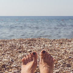 Women's feet with black manicures on the beach