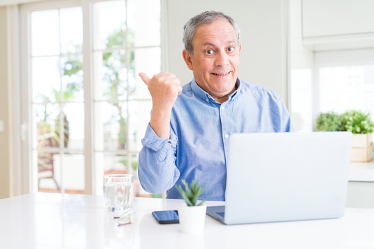 Handsome senior man using computer laptop working on internet pointing and showing with thumb up to the side with happy face smiling