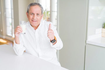 Fototapeta premium Handsome senior man drinking a glass of fresh milk at breakfast happy with big smile doing ok sign, thumb up with fingers, excellent sign