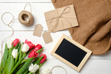 Bouquet of tulips flowers, kraft envelope, twine, tags, burlap on white wooden table. Vintage greeting card for womans day, mothers day, birthday, easter. Rustic background, flat lay, above view.