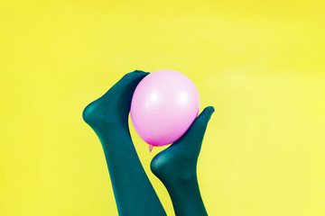 Green legs of a woman holding a pink balloon against a yellow wall