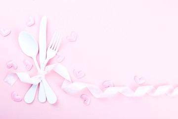 Festive table setting for Valentines Day with fork, knife and hearts on pink pastel background.Set of silverware .Romantic dinner. Space for text. Top view
