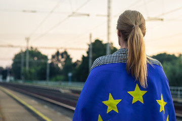 Woman with European Union flag waiting for train on railroad station