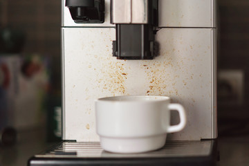 white cup on a dirty coffee machine in the kitchen or office, close-up