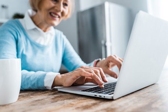selective focus of smiling senior woman typing on laptop at home