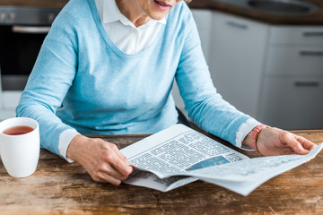 cropped view of senior woman reading newspaper at home