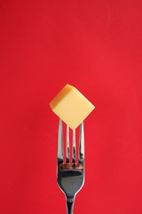 Yellow cheese on a fork. Red background with copy space