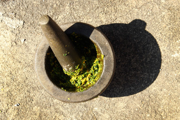 Cooking Thai green Chili paste in stone mortar with pestle on a street.