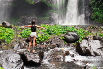 a young girl standing on the rocks admires the natural waterfall .the view from the back .
