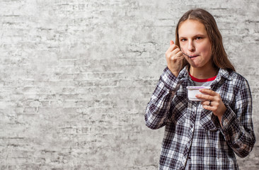 portrait of young teenager brunette girl with long hair eat blueberry yogurt on gray wall background with copy space.