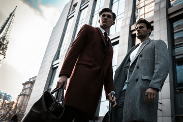 Two fashion men models posing on city street. Wearing in classic and casual closes. Suit, coat,...