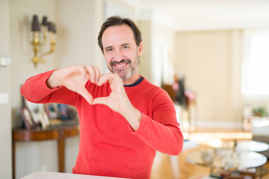 Handsome middle age man at home smiling in love showing heart symbol and shape with hands. Romantic concept.