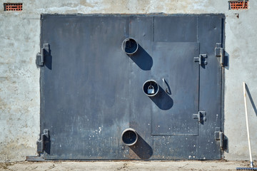 Metal garage door with round protections for padlocks. The wall of the garage is concrete and plastered. Top ventilation grilles. Rake for cleaning the area in front of the building.