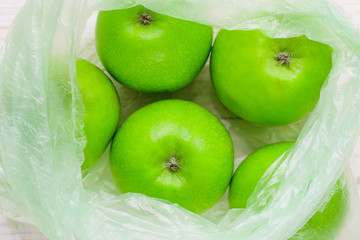 Fresh green apples in plastic bag on wooden table. environmental concept of non-ecological use of plastic