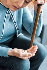 cropped view of sick senior woman with walking stick holding medicine in hand