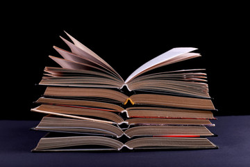 Open books are stacked on the desk, on a black background, isolate. Difficult homework at school, a mountain of knowledge.