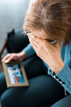 senior woman covering face with hand and crying while looking at picture frame