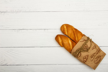 Fresh bread wrapped in old newspaper on a white wooden table. Top view with space for your text.