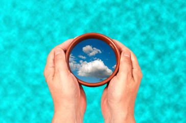 in the hands of a cup with a reflection of clouds on the background of water