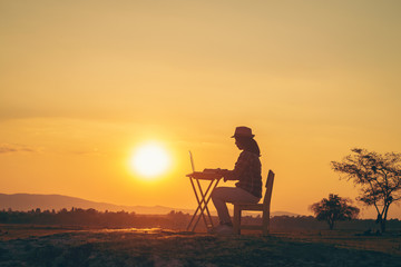 A young woman sitting in an outdoor work at sunset