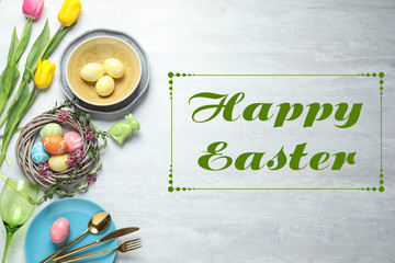Festive table setting and text Happy Easter on wooden background, top view