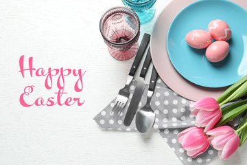 Festive table setting and text Happy Easter on wooden background, top view