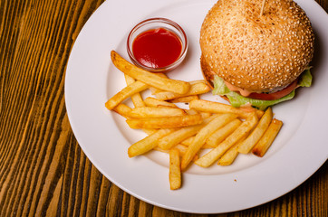 Tasty burger and french fries on plate, on wooden table background. Unhealthy food concept