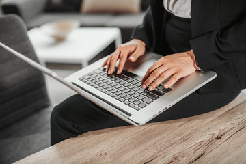 A picture of laptop. Girl holds it on her lap. She has her fingers on its keyboard. Woman types. She works