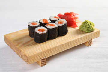 Serving board with tasty sushi rolls on white table. Food delivery