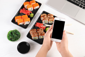 Woman with mobile phone and sushi rolls at table, space for text. Food delivery