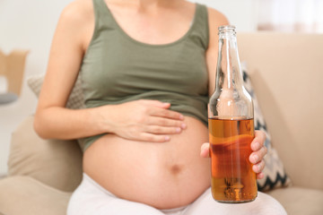 Pregnant woman with bottle of whiskey at home. Alcohol addiction