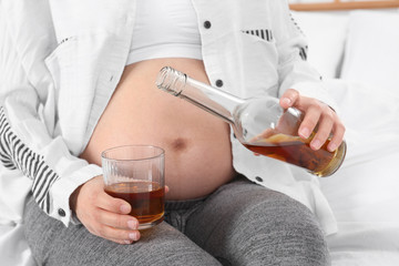 Pregnant woman pouring whiskey into glass at home. Alcohol addiction