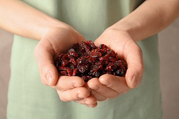 Woman holding handful of tasty cranberries on color background, closeup. Dried fruits as healthy snack