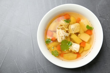 Homemade chicken soup in dish on grey background, top view with space for text