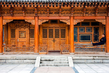 Traditional Wooden Chinese Architecture Of The House And A Sitting Man.