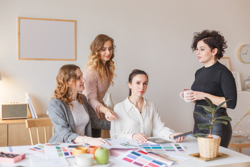 Team of female designersduscussing a new project using color palette sitting at desk in modern...