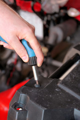 Automotive mechanic and master is holding screwing a screw with blue screw driver in automechanics workshop. Mechanician hands of car mechanic with screw gun in auto repair service center, car garage.