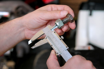 Worker with tools in hands. Mechanic is checking and measuring screw size with stainless steel caliper in automechanics workshop, car garage. Hands of mechanic holding steel screw using steel caliper.