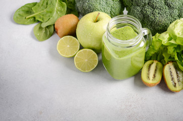 Fresh green smoothie in a jar with ingredients on a gray concrete background, selective focus.