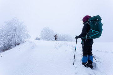 Fototapeta na wymiar Young couple trekking together with their dog through the frozen mountains in Romania