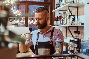 Handsome barista in apron drinking coffee during lunch break standing behind the counter in the coffee shop